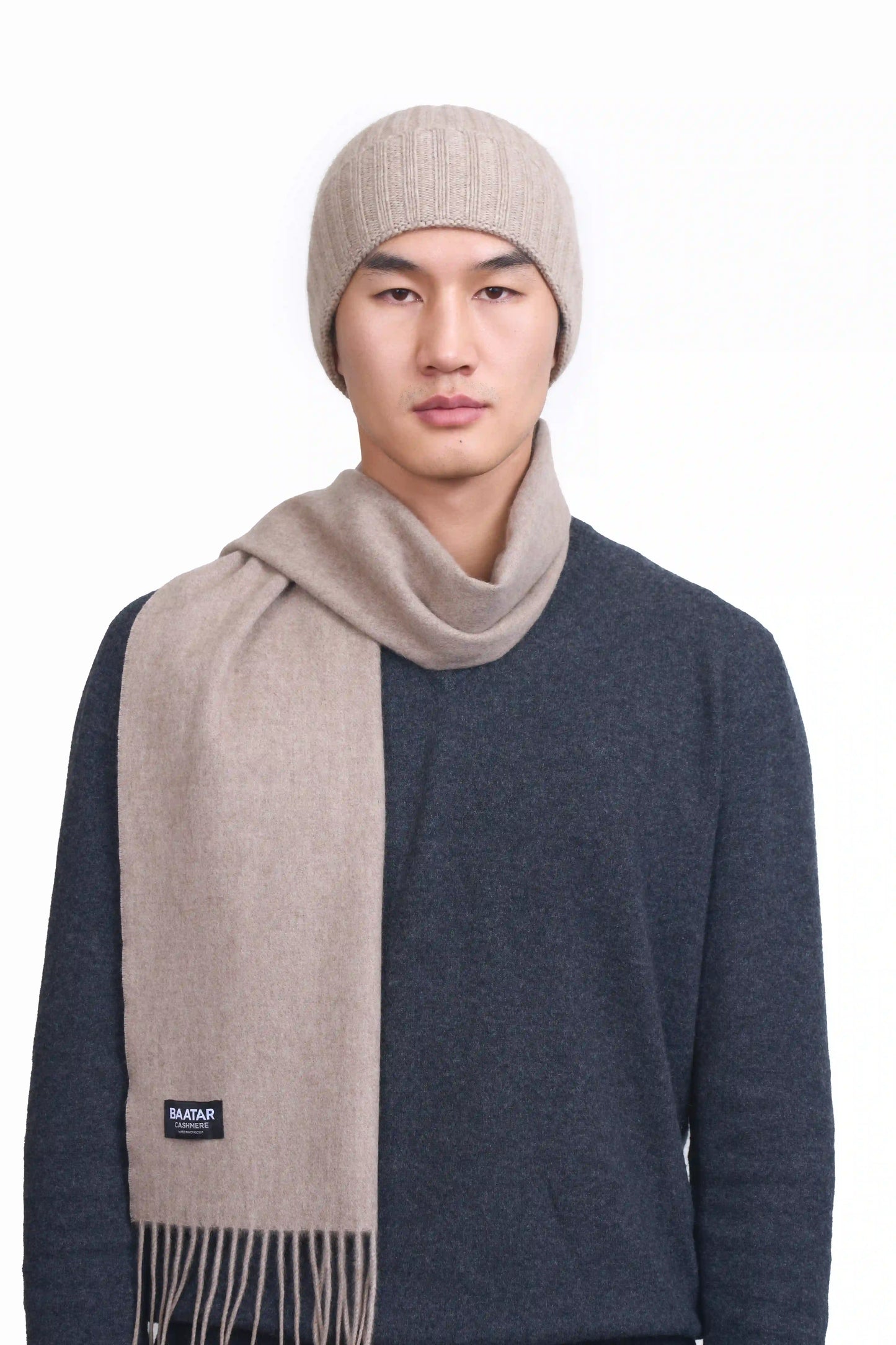 Mongolian male model wearing a soft natural beige cashmere beanie and scarf set, highlighting the luxurious texture and elegant design against a neutral background