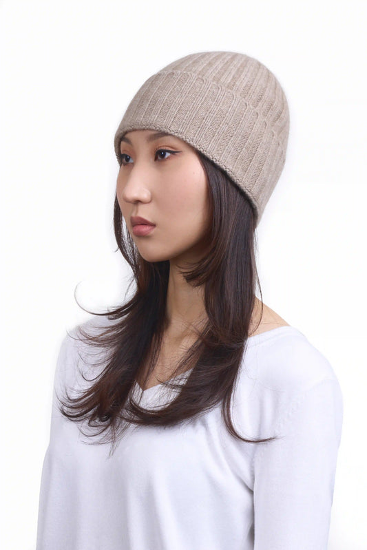 Mongolian female model in 3/4 view wearing a soft natural beige cashmere beanie, highlighting the luxurious texture and elegant design against a neutral background