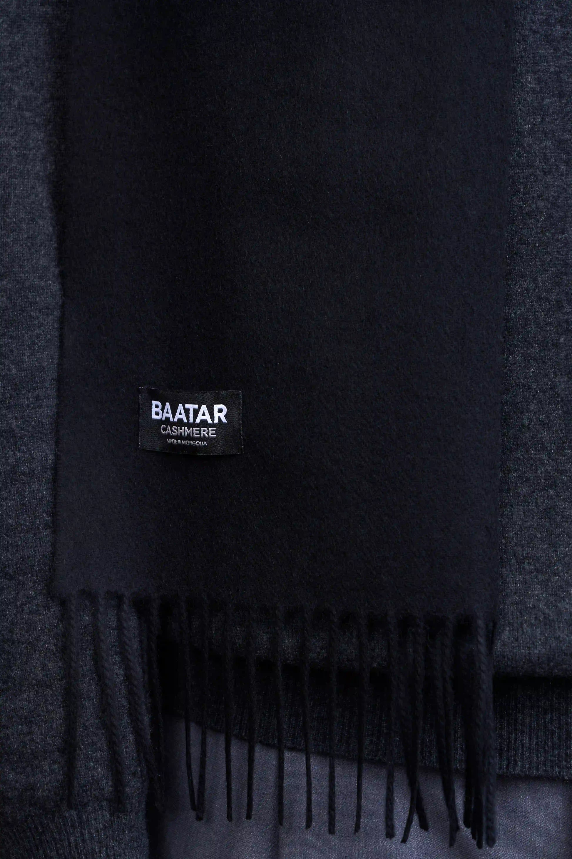 Warm black Mongolian cashmere scarf draped elegantly on a gray sweater to highlight its softness and versatility.