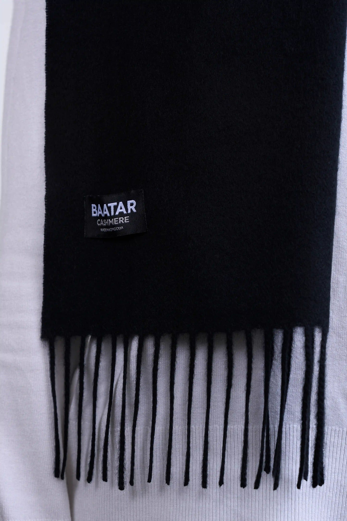 Warm black Mongolian cashmere scarf draped elegantly on a white sweater to highlight its softness and versatility.