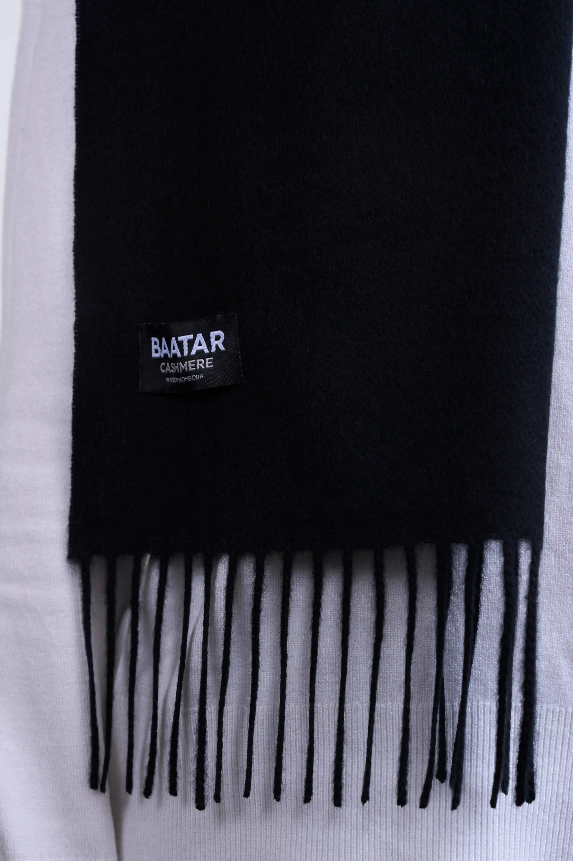 Warm black Mongolian cashmere scarf draped elegantly on a white sweater to highlight its softness and versatility.