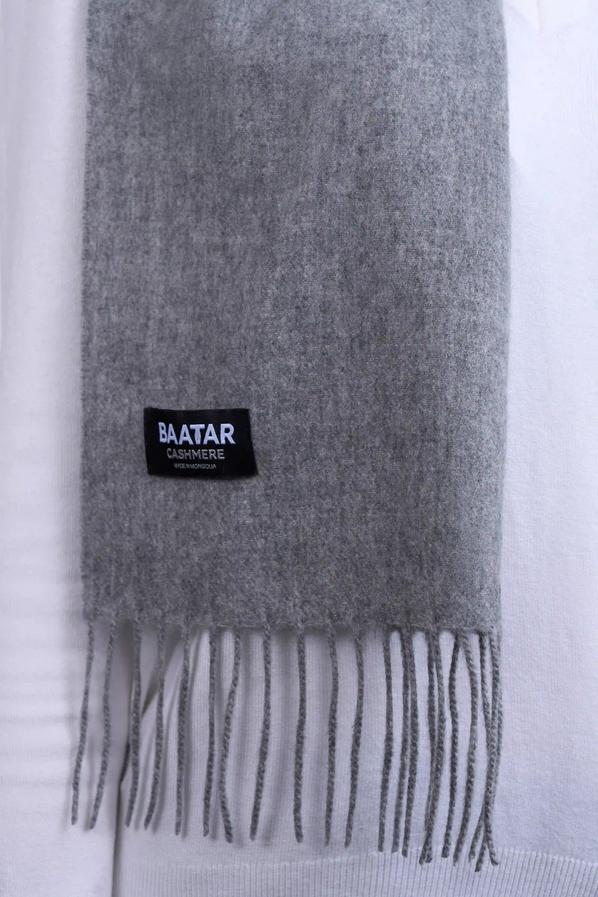 Warm light gray Mongolian cashmere scarf draped elegantly on a white sweater to highlight its softness and versatility.