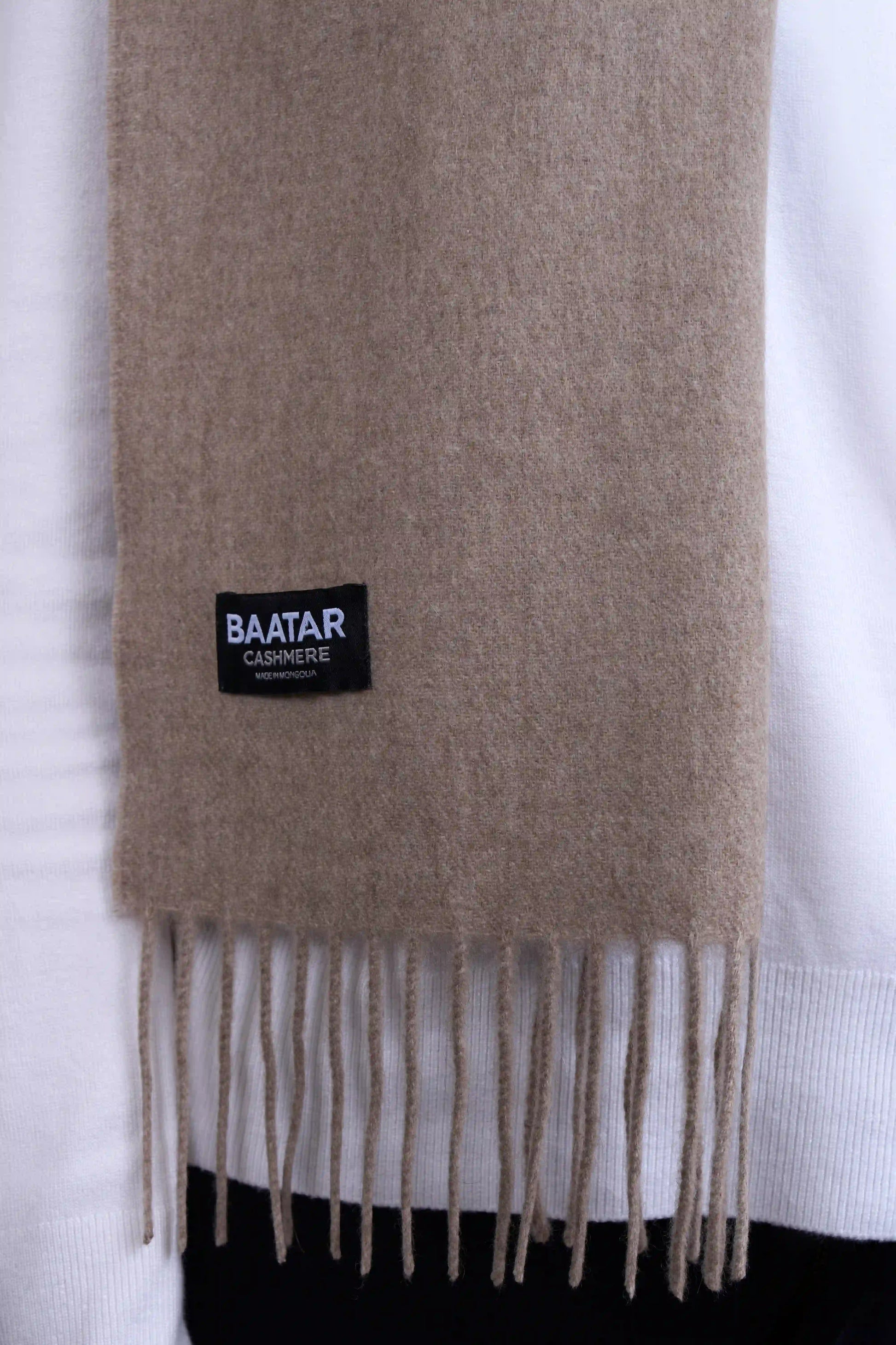 Warm natural beige Mongolian cashmere scarf draped elegantly on a white sweater to highlight its softness and versatility.